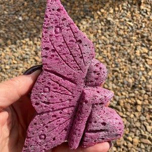 Könnte beinhalten: Eine rosafarbene Feenfigur aus porösem Stein. Die Fee hat Flügel und ein fließendes Kleid. Der Stein hat eine raue Textur und ein gesprenkeltes Aussehen.