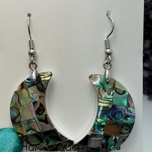 May include: A pair of crescent-shaped earrings with iridescent abalone shell inlays. The earrings have a mosaic pattern of green, blue, and brown hues. The ear wires are silver-colored.
