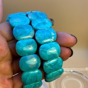 May include: Two bracelets composed of polished, rectangular, bright turquoise-blue stones with natural white marbling and variations in color. The stones are smooth, rounded at the edges, and strung together to form a flexible, continuous band.