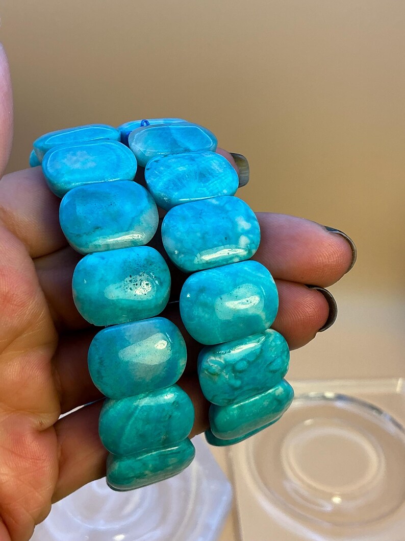 May include: Two bracelets composed of polished, rectangular, bright turquoise-blue stones with natural white marbling and variations in color. The stones are smooth, rounded at the edges, and strung together to form a flexible, continuous band.
