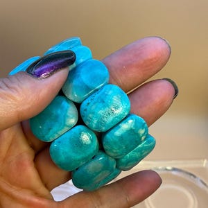 May include: A stretch bracelet composed of multiple smooth, polished, rectangular turquoise-colored stones with natural white veining and variations in blue and green hues, arranged in a multi-strand configuration.