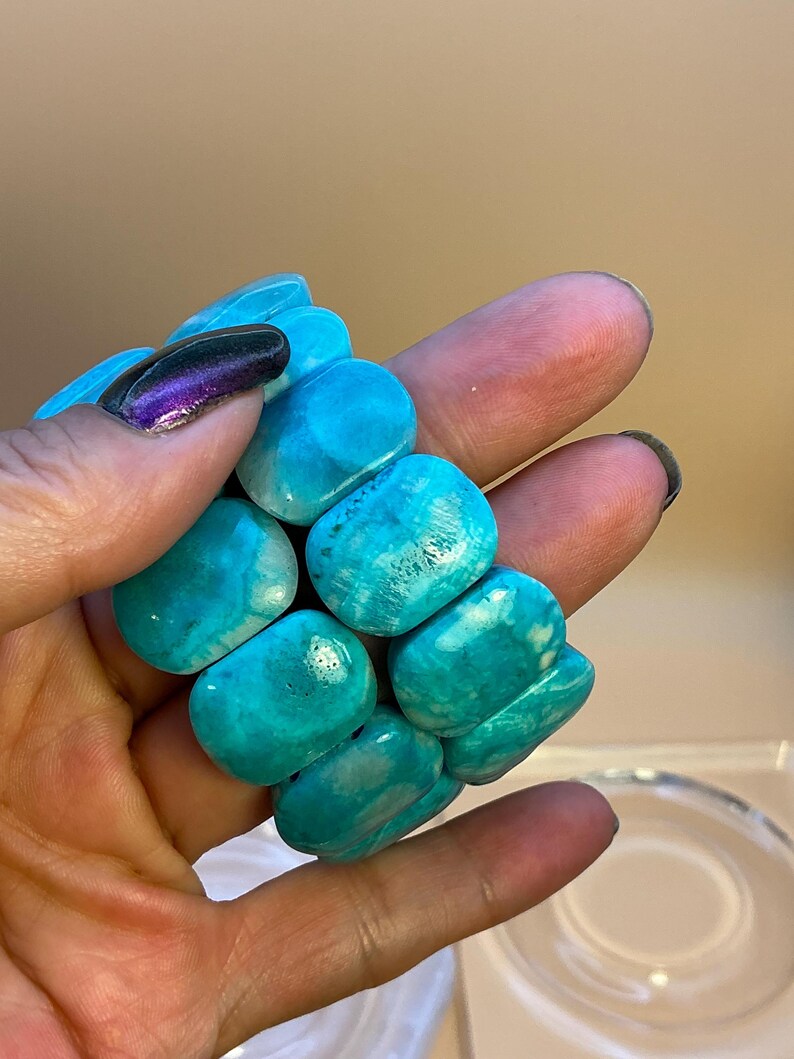 May include: A stretch bracelet composed of multiple smooth, polished, rectangular turquoise-colored stones with natural white veining and variations in blue and green hues, arranged in a multi-strand configuration.