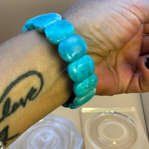 May include: A stretch bracelet composed of smooth, polished, rectangular turquoise-colored beads. The beads feature natural variations in color, ranging from bright cyan to deeper blue tones, and are strung together to form a continuous circular band.