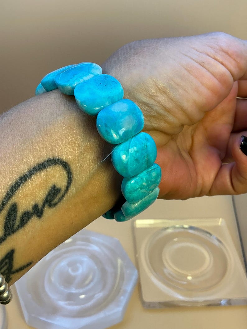 May include: A stretch bracelet composed of smooth, polished, rectangular turquoise-colored beads. The beads feature natural variations in color, ranging from bright cyan to deeper blue tones, and are strung together to form a continuous circular band.