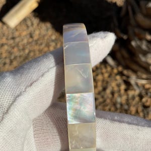 Puede incluir: Un brazalete blanco de nácar con un diseño de azulejos cuadrados.