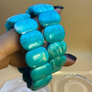 May include: A stretch bracelet composed of smooth, rectangular turquoise-colored beads with natural veining and variations in shade. The beads are arranged in a continuous loop, showcasing a polished finish and a vibrant, saturated blue-green hue.