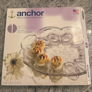 Peut inclure: Une assiette à œufs en verre transparent avec un motif floral, contenant des œufs farcis. La boîte indique "anchor" et "Raise a Glass to Planet Earth". L'assiette mesure 30,5 cm de diamètre.