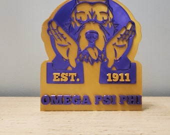 May include: A gold and purple 3D printed figurine of a dog's head with the text "EST. 1911 OMEGA PSI PHI" on the base.
