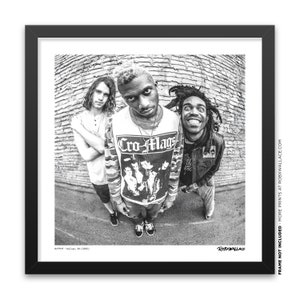 May include: Black and white photo of three people standing in front of a brick wall. The person in the middle is wearing a black and white shirt with the words "Cro-Mags" printed on it. The person on the left is wearing a plain shirt and the person on the right is wearing a jacket and striped pants.