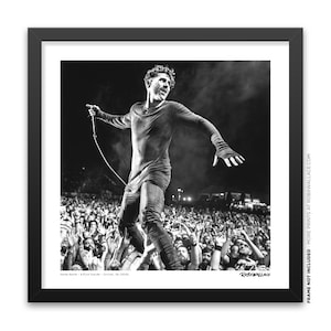 Könnte beinhalten: Schwarzweißfoto eines Musikers, der auf einer Bühne vor einer großen Menge auftritt. Der Musiker trägt ein schwarzes Langarmshirt und eine schwarze Hose. Die Menge jubelt und hält die Hände in die Luft. Das Foto ist mit "RobxWallace" signiert.