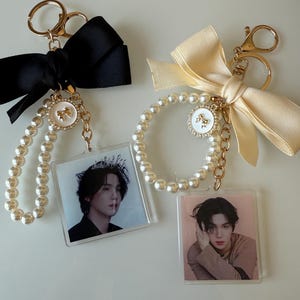 May include: Two keychains with gold-colored hardware, pearl bead accents, and a clear photo insert. One keychain has a black satin bow, the other a cream-colored bow. Each features a portrait.