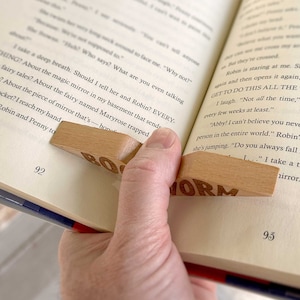 May include: A wooden bookmark with the words "BOOKWORM" engraved on it. The bookmark is being used to hold open a book with the page number 92 visible.