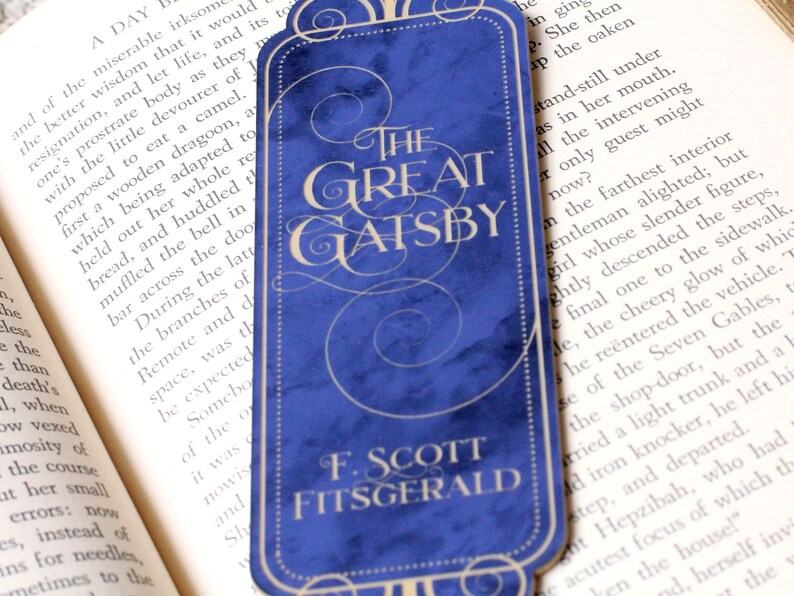 Op de afbeelding: Een blauwe bladwijzer met de titel "The Great Gatsby" van F. Scott Fitzgerald. De bladwijzer heeft een decoratief ontwerp met een draaiend patroon.