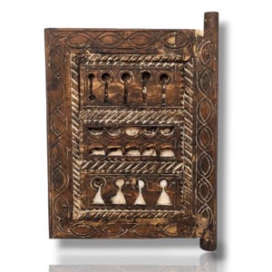May include: A rectangular dark brown wooden panel featuring intricate hand-carved geometric patterns, including oval borders, diagonal rope-like textures, and three horizontal rows of cut-out shapes filled with white inlay material.