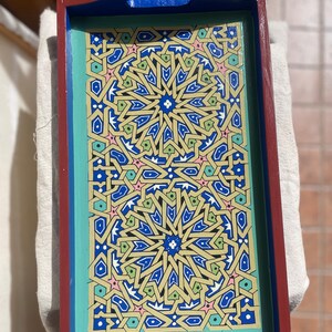 May include: A wooden serving tray with a blue and green border and a geometric pattern in shades of blue, green, yellow, pink, and white.