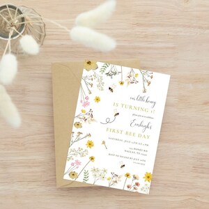 Puede incluir: Una tarjeta de invitaci&oacute;n blanca con un borde floral y un dise&ntilde;o de abeja. El texto en la tarjeta dice "&iexcl;nuestro peque&ntilde;o miel cumple 1!" y "&iexcl;Primer d&iacute;a de la abeja!".