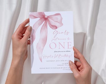 May include: A white invitation card featuring a pink watercolour bow and the text "Girls just wanna be ONE" is held. The card announces Hazel's 1st birthday, including the date, time, and location in Dallas, TX.