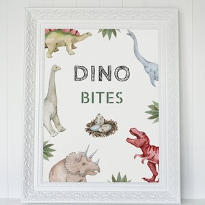 May include: A white framed print with a white background and colorful illustrations of dinosaurs. The text "DINO BITES" is written in green and black letters.