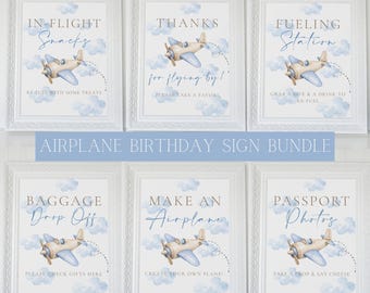 May include: A set of six framed signs with a vintage airplane theme. Each sign features a watercolor airplane illustration and text such as "In-Flight Snacks" and "Passport Photos." The signs are in white frames with a blue and white color scheme.