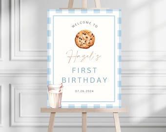 May include: A blue and white gingham patterned welcome sign for a first birthday party. The sign says "Welcome to Hazel's First Birthday 07.26.2024" and features a chocolate chip cookie and a glass of milk with a straw.