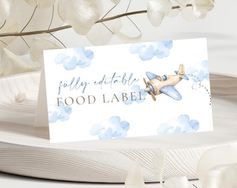 Może przedstawiać: Złożona biała etykieta na żywność z niebieskim i brązowym napisem "fully editable FOOD LABEL". Etykieta zawiera akwarelową ilustrację jasnoniebieskiego samolotu i puszystych niebieskich chmur.
