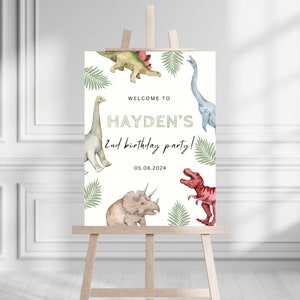 May include: Welcome to Hayden's 2nd birthday party! A white sign with green leaves and colourful dinosaur illustrations. The date 05.06.2024 is printed at the bottom.