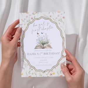 May include: A floral-themed invitation card with the text "hazel's first chapter" and "HAZEL'S 1ST BIRTHDAY!". The design features an open book with flowers and butterflies, set against a white background with a decorative border.