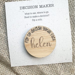 Może przedstawiać: Drewniana moneta decyzyjna z wygrawerowanym imieniem "helen". Moneta znajduje się na białej karcie z napisem "DECISION MAKER" i instrukcjami. Moneta głosi "flip to decide your fate".