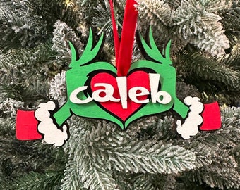 Puede incluir: Adorno navideño de madera verde y rojo con forma de mano haciendo un corazón con el nombre "Caleb" escrito dentro del corazón.