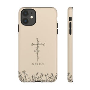 May include: A beige phone case with a black outline and a floral cross design. The text "John 15:5" is printed below the cross. The case has a black camera cutout and a black outline around the edges.