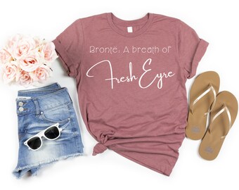 May include: A mauve t-shirt with the text "Brontë: A breath of Fresh Eyre" in white script.
