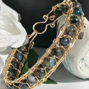 May include: A gold wire wrapped bracelet with blue and green gemstone beads. The bracelet has a clasp closure.