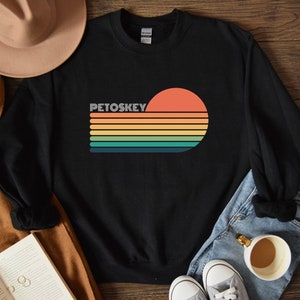 May include: Black sweatshirt with a retro sunset graphic and the text "Petoskey" in white.