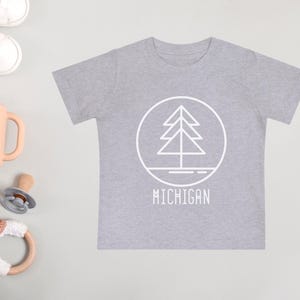 May include: A gray t-shirt with a white outline of a pine tree inside a circle and the word "MICHIGAN" underneath.