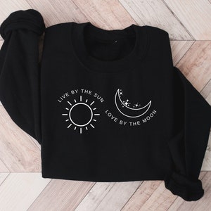 May include: Black sweatshirt with a white graphic design of a sun and moon with the text "Live by the sun, love by the moon."