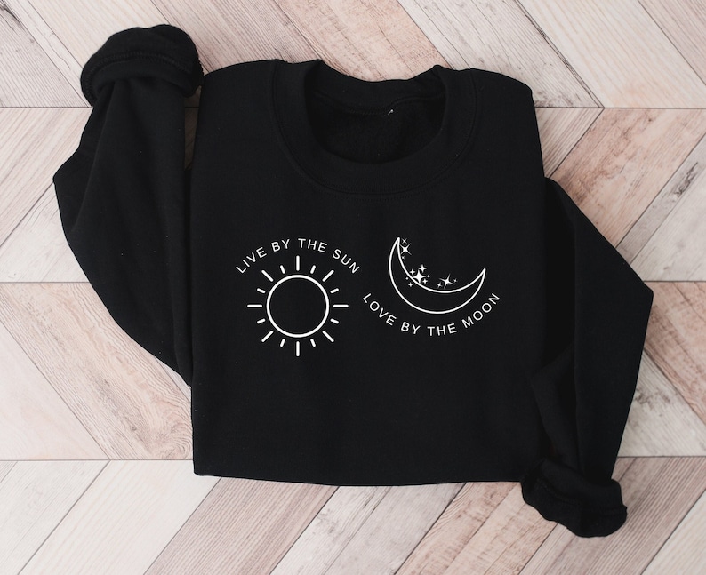 May include: Black sweatshirt with a white graphic design of a sun and moon with the text "Live by the sun, love by the moon."