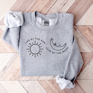 May include: Gray sweatshirt with the text "Live by the sun, love by the moon" and a sun and moon graphic.
