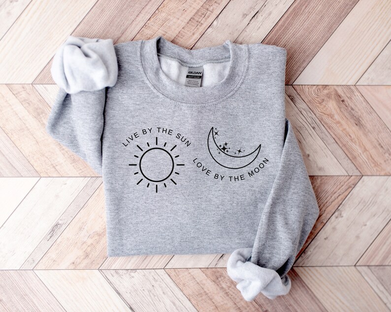 May include: Gray sweatshirt with the text "Live by the sun, love by the moon" and a sun and moon graphic.