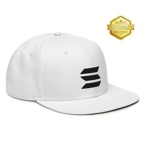 Op de afbeelding: Een witte baseballcap met een platte klep. De pet heeft een zwart geometrisch ontwerp aan de zijkant en een goudkleurige "Exclusive High Quality Best Choice" badge.