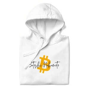 May include: White hoodie with a drawstring and a gold Bitcoin symbol and the words "Satoshi Nakamoto" in black script. The hoodie is folded and has a front pocket.