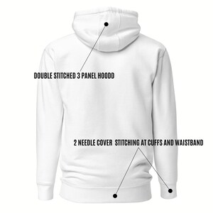 May include: A white hoodie with the text "DOUBLE STITCHED 3 PANEL HOODD" and "2 NEEDLE COVER STITCHING AT CUFFS AND WAISTBAND". The hoodie features a hood and ribbed cuffs and waistband.