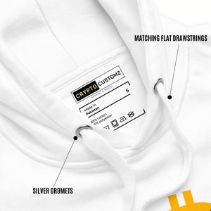 May include: White hoodie with a drawstring hood. Features silver grommets and matching flat drawstrings. The tag reads "CRYPTO CUSTOMZ APPAREL & MERCH" and "Made in Pakistan". The hoodie is made of 65% cotton and 35% polyester.