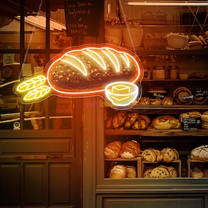 May include: A neon sign in the shape of a loaf of bread with wheat and butter, hanging in front of a bakery. The sign is outlined in orange with bright yellow accents. Shelves display various baked goods, including loaves, rolls, and pastries.