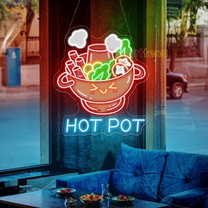 May include: A neon sign with a cartoon hot pot design, featuring a smiling bowl with vegetables and noodles. The sign is outlined in red and white, with the words "HOT POT" in blue neon. The sign is hanging in a window.