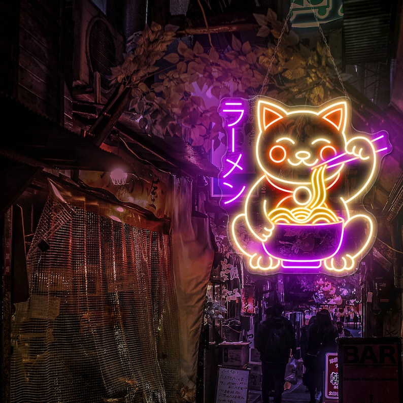 Puede incluir: Letrero de ne&oacute;n de un gato de dibujos animados sosteniendo un taz&oacute;n de fideos ramen con palillos. El letrero est&aacute; iluminado en rosa y amarillo y dice "Ramen" en caracteres japoneses.