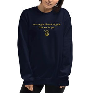 May include: Navy blue sweatshirt with gold text that reads "one single thread of gold tied me to you" and a gold illustration of two hands holding each other. The sweatshirt is a solid color and has a crew neck.