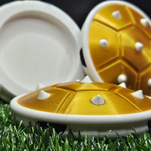 May include: Three white and gold plastic toy shells with spikes. The shells are stacked on top of each other.