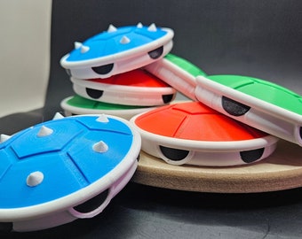 May include: A stack of four colorful, spiky, plastic turtle shells. The shells are blue, red, green, and blue. The shells are all the same size and shape, and they are all stacked on top of each other. The shells are on a wooden surface.