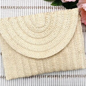 May include: A woven straw clutch with a flap closure. The clutch is a light beige color and has a textured surface. The flap has a semi-circular design. The clutch has a gold-colored chain strap.