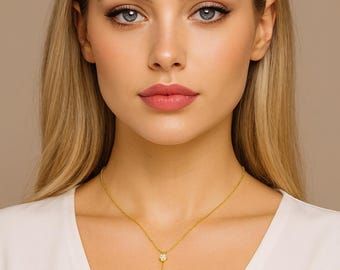May include: A gold-colored necklace with two clear, sparkling gemstones. The necklace has a delicate chain and a Y-shaped design, with one gemstone at the top and a larger, triangular gemstone at the bottom. The woman is wearing a white top.